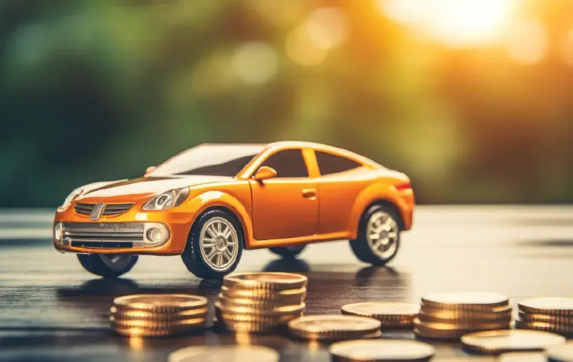 A glossy orange toy car on a table, surrounded by stacked coins, with a warm, soft sunlight backdrop.